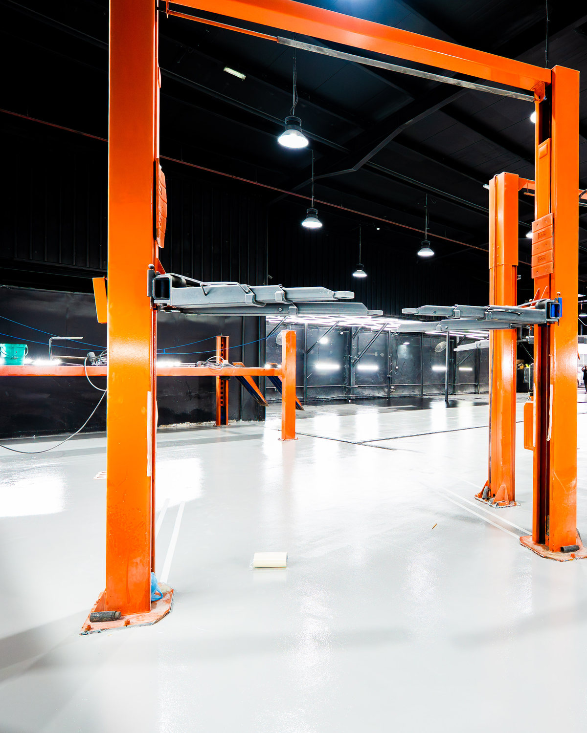 An orange two-post vehicle lift standing empty on the pale epoxy floor of the Top Challenger workshop in Mussafah Industrial, Abu Dhabi, with further lifts receding behind it under a black-clad roof