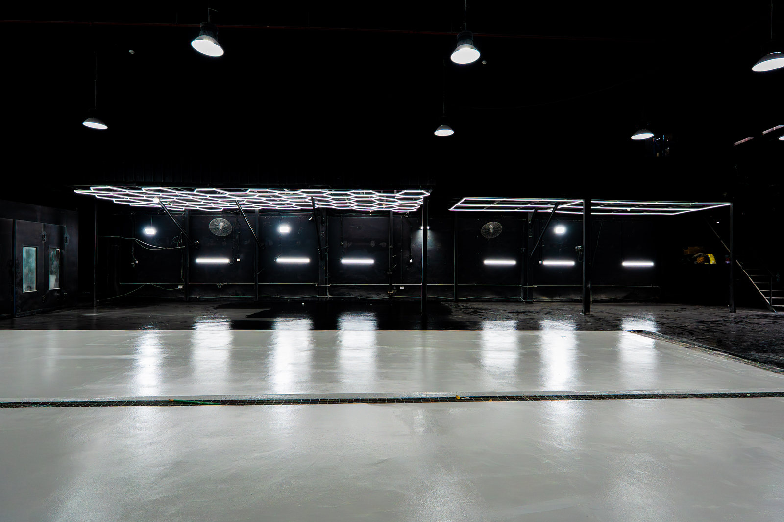Work bays along the wall of the Top Challenger workshop in Mussafah Industrial, Abu Dhabi, under hexagonal LED light rigs, with wall fans between the bays and a pale epoxy floor in front of them