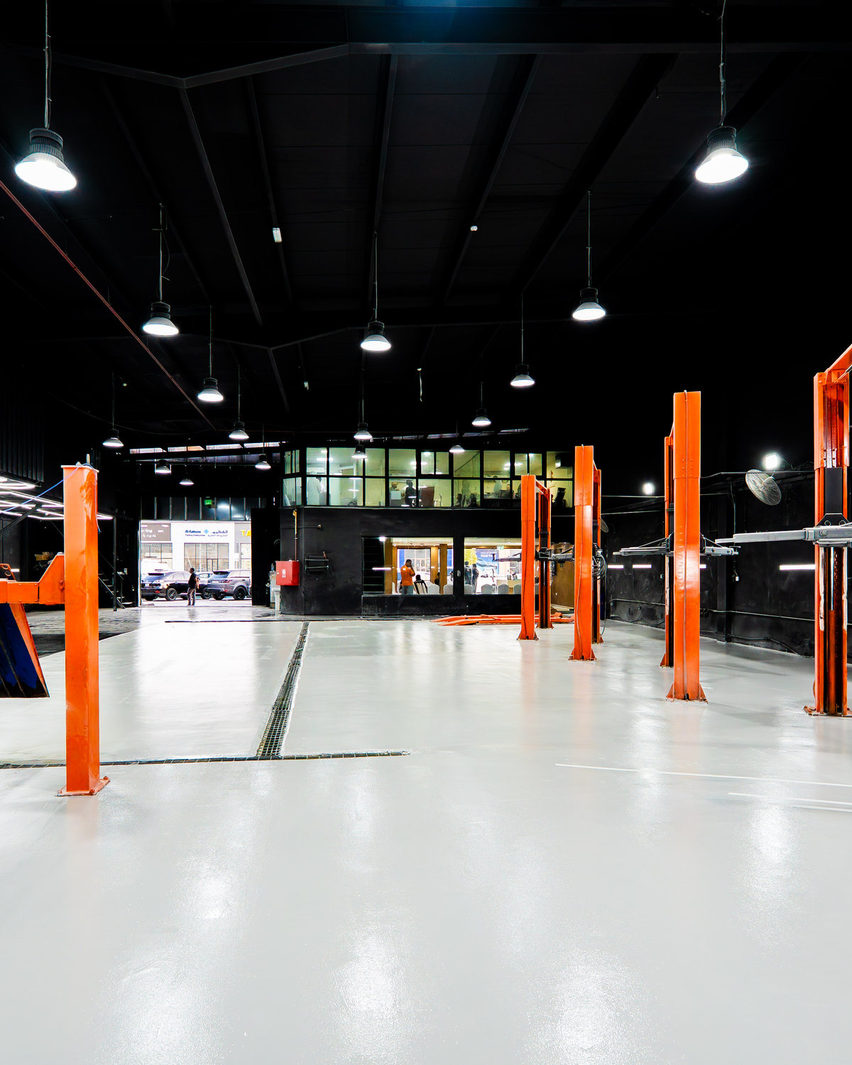 The main floor of the Top Challenger workshop in Mussafah Industrial, Abu Dhabi, looking the length of the bay to a two-storey glazed office above a reception area, with a four-post lift on the left and two-post lifts along the right