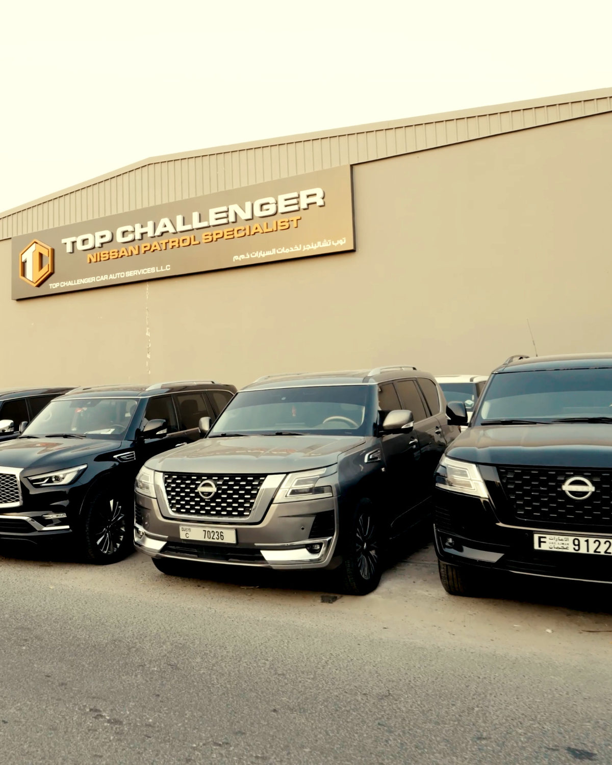The front of the Top Challenger workshop in Ras Al Khor Industrial Area 1, Dubai: the sign reading TOP CHALLENGER, NISSAN PATROL SPECIALIST above a row of black and grey SUVs parked along the street, two Nissan Patrols nearest the camera